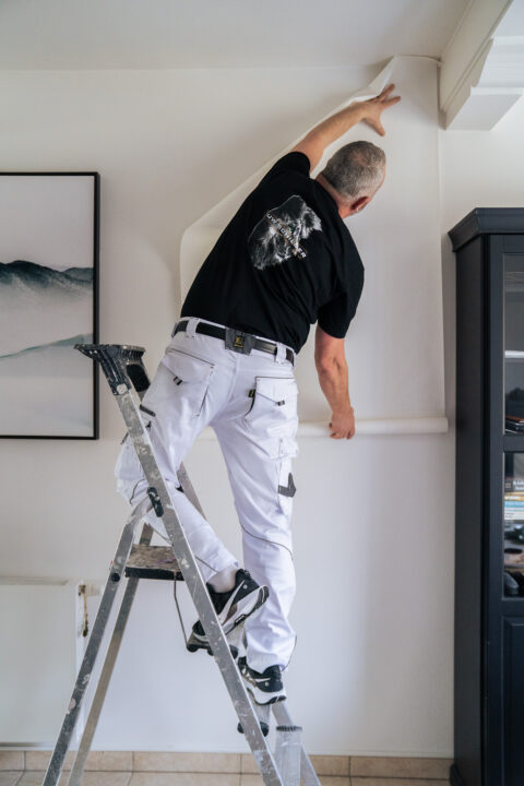 Pieter hangt behang op een ladder